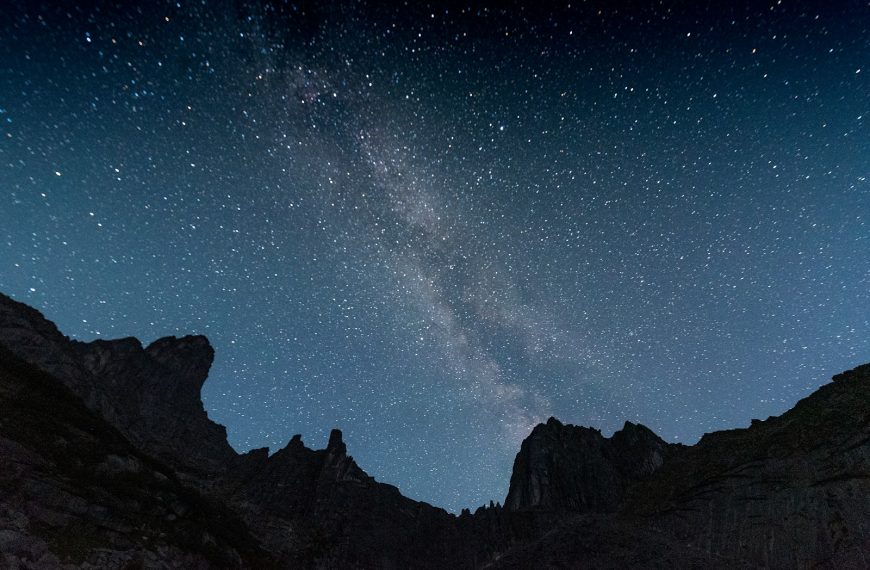The night sky is filled with stars above a mountain range