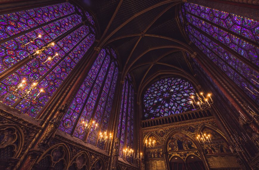 Interior of Sainte-Chapelle in Paris, showcasing its iconic stained glass windows with intricate purple and gold designs under soaring Gothic arches.