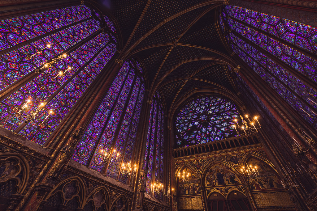 Interior of Sainte-Chapelle in Paris, showcasing its iconic stained glass windows with intricate purple and gold designs under soaring Gothic arches.