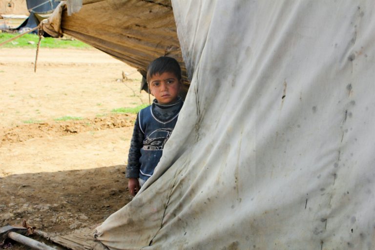 A young boy standing in front of a tent in Syria